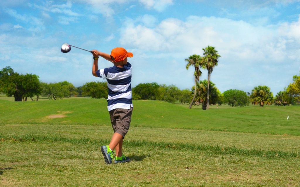 Young golfer taking a swing on golf course green